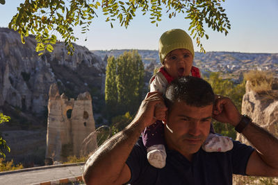 Father carrying baby on shoulder against mountain