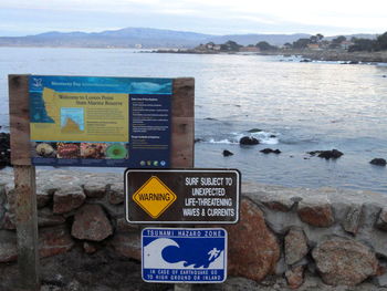 Information sign by sea against sky