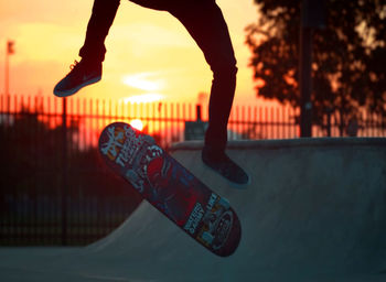 Low section of man performing stunt on skateboard in park during sunset