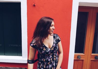 Young woman looking away while standing against wall