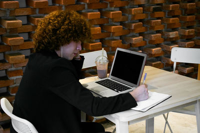 Non-binary person is writing in a notebook while is working at a cafeteria