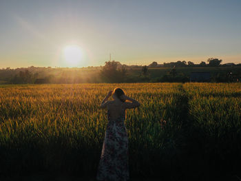 Rear view of woman standing at farm against sky during sunset