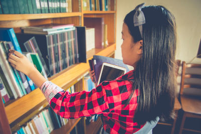 Girl holding books and digital tablet by shelf