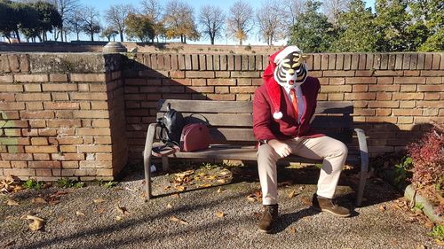 Full length of man sitting on seat against brick wall