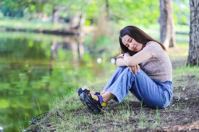 Full length of woman sitting on grass by lake