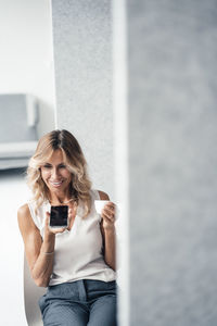 Businesswoman with coffee cup talking on speaker phone sitting at office