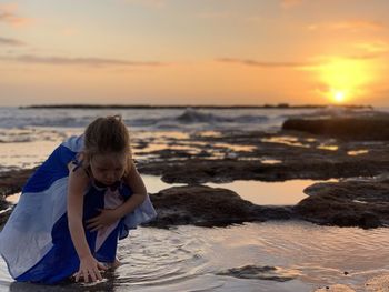 Rear view of a girl on beach against sky during sunset