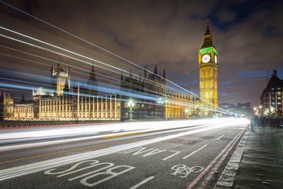 Light trails on road by big ben against sky in city at night