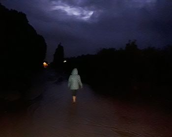 Rear view of woman walking on illuminated road against sky at night