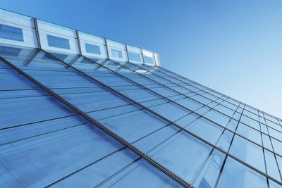 Low angle view of glass building against blue sky