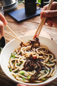 Close-up of person holding noodles in bowl on table