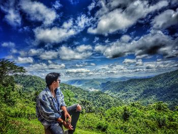 Full length of young man sitting on land against sky