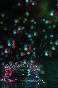 Close-up of splashing droplet against illuminated christmas lights