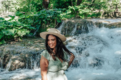 Portrait of young woman standing against waterfall