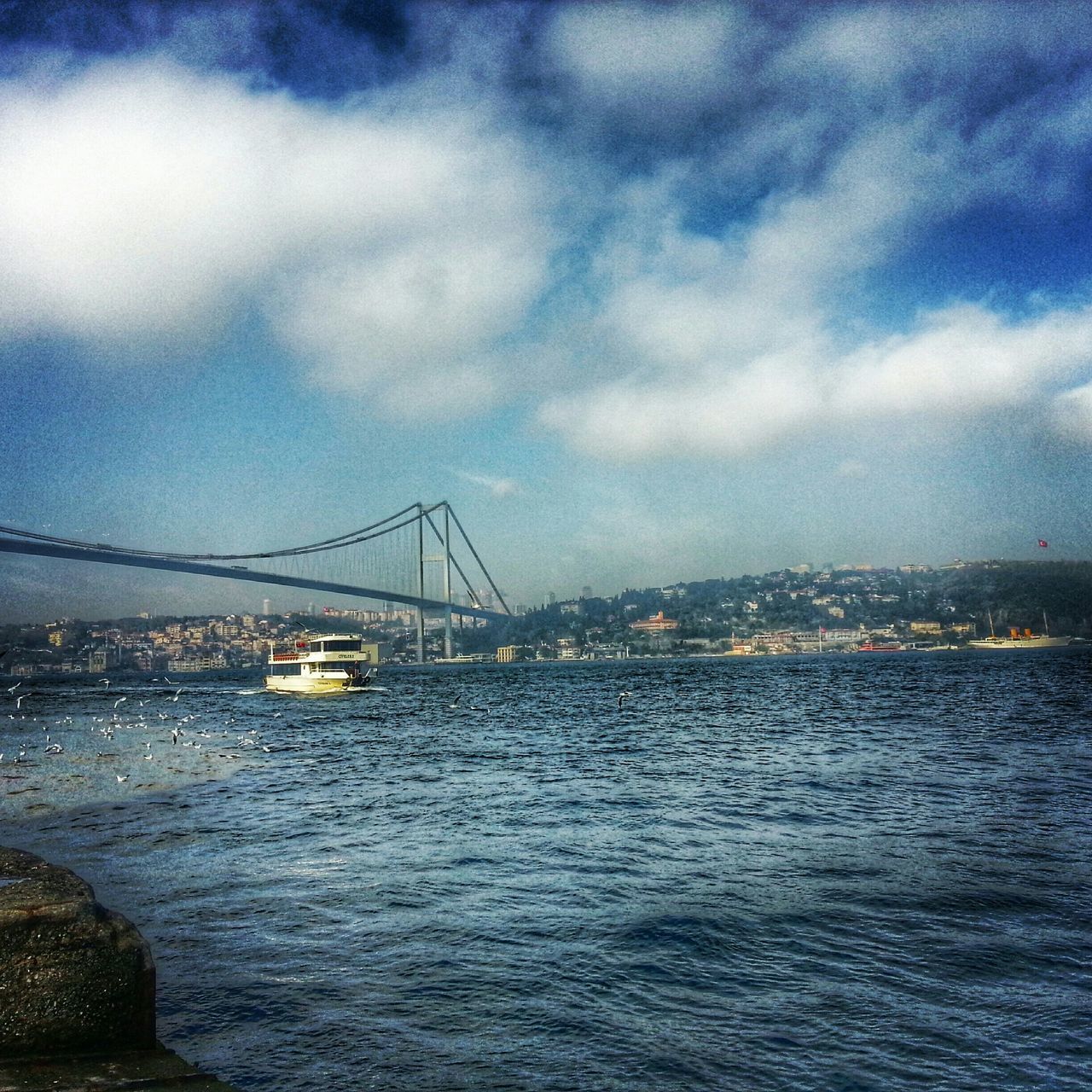 water, connection, architecture, waterfront, sky, built structure, bridge - man made structure, transportation, river, cloud - sky, sea, cloudy, engineering, city, suspension bridge, bridge, cloud, rippled, nautical vessel, travel destinations