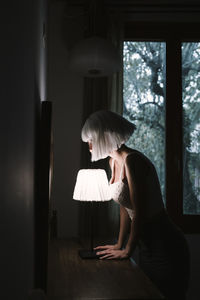 Side view of woman sitting on window at home