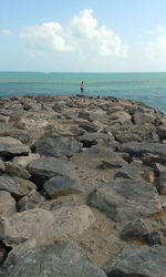 Rear view of man standing on rock by sea against sky