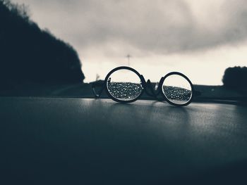 Close-up of eyeglasses on glass against sky