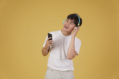 Young woman using phone while standing against yellow background