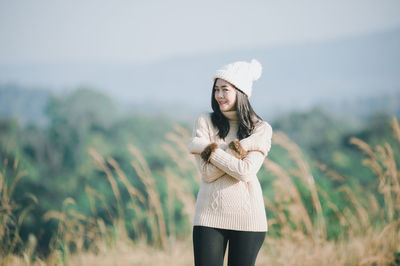 Portrait of smiling young woman standing against plants and sky