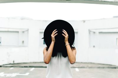 Woman standing on street and covering face with hat