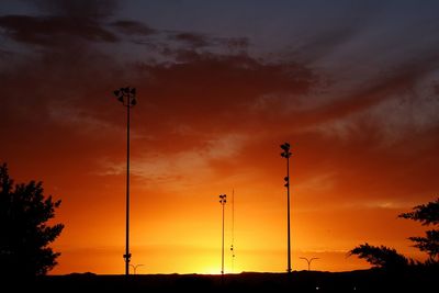 Low angle view of silhouette street lights against orange sky