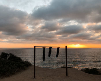 Wooden posts on beach against sky during sunset