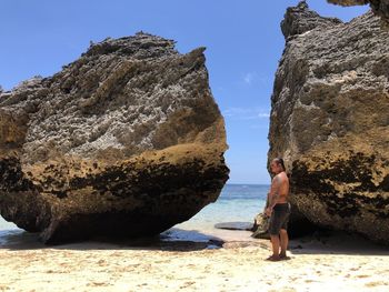 Man standing on rock by sea against sky