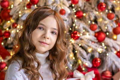 Portrait of a happy girl looking at the camera, posing against the background of a christmas tree.