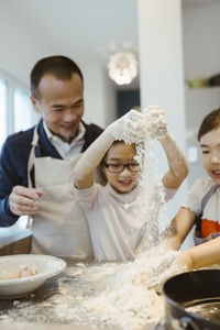 Playful girls kneading dough with father in kitchen at home