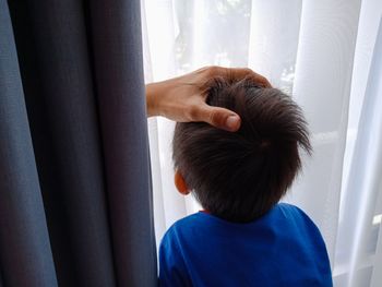 Cropped hand on son head by window at home