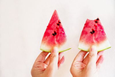 Close-up of hand holding strawberry over white background