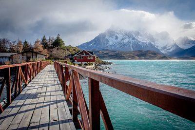 Diminishing perspective of footbridge over river against cloudy sky