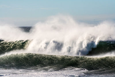 Scenic view of waves breaking against sea