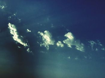 Low angle view of sunlight streaming through clouds