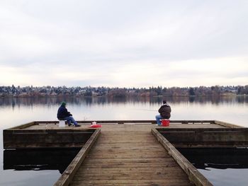 Full length of people fishing on pier by lake against sky