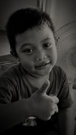 Portrait of cute boy showing thumbs up while sitting at home