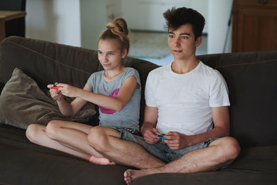 Siblings playing video game on couch at home