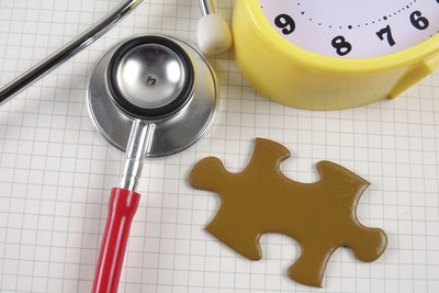 High angle view of stethoscope with alarm clock and jigsaw puzzle piece on notebook