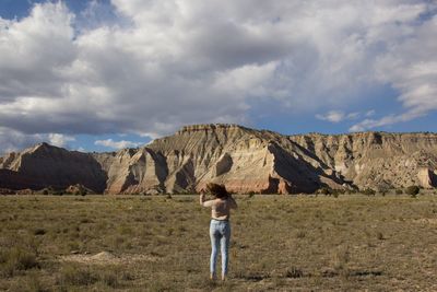 Full length rear view of woman standing on field by rocky mountains against cloudy sky at kodachrome basin state park