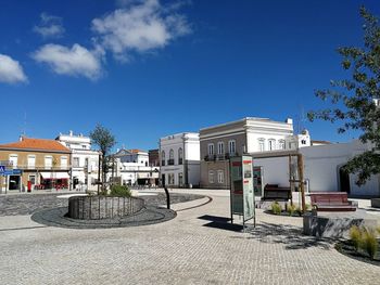 Buildings by street against blue sky