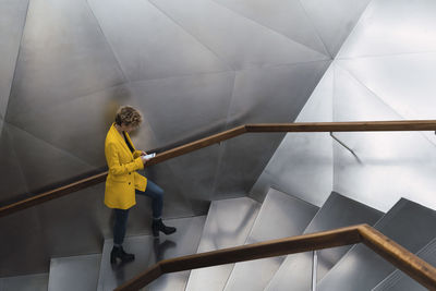 Young businesswoman using smart phone walking on staircase at office