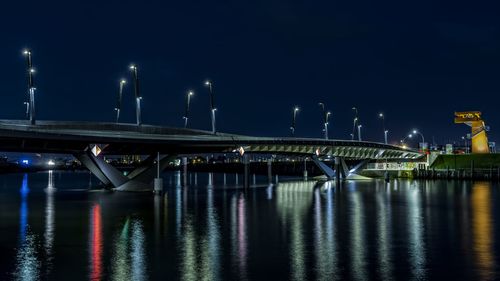 Illuminated bridge over river against sky at night