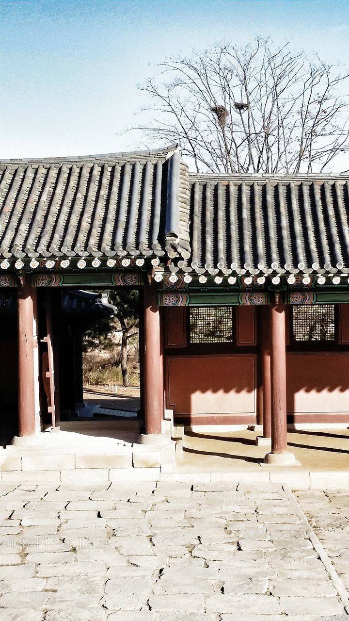 built structure, architecture, building exterior, text, clear sky, western script, roof, sky, day, outdoors, wood - material, tree, communication, no people, gate, sunlight, in a row, low angle view, house, old