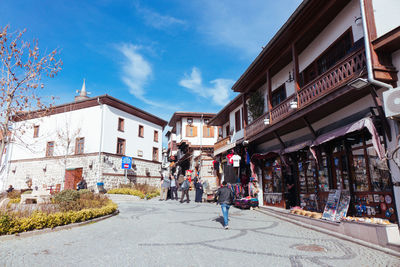 People walking on road amidst buildings in city against sky