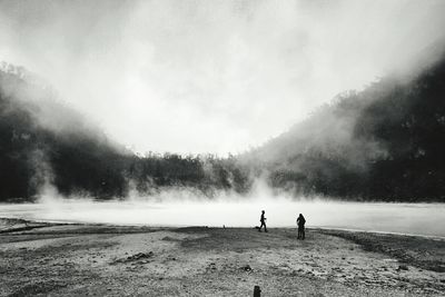 People by hot spring lake against sky