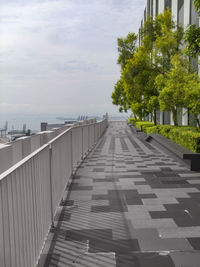 Empty footpath by street in city against sky