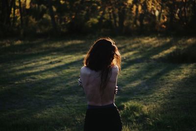 Rear view of shirtless woman standing on grass field in forest