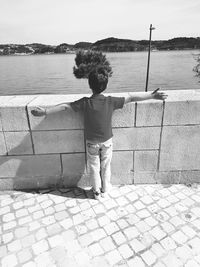 Rear view of boy standing on retaining wall against sea