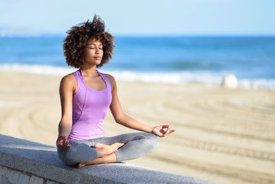 Young woman meditating on retaining wall at beach